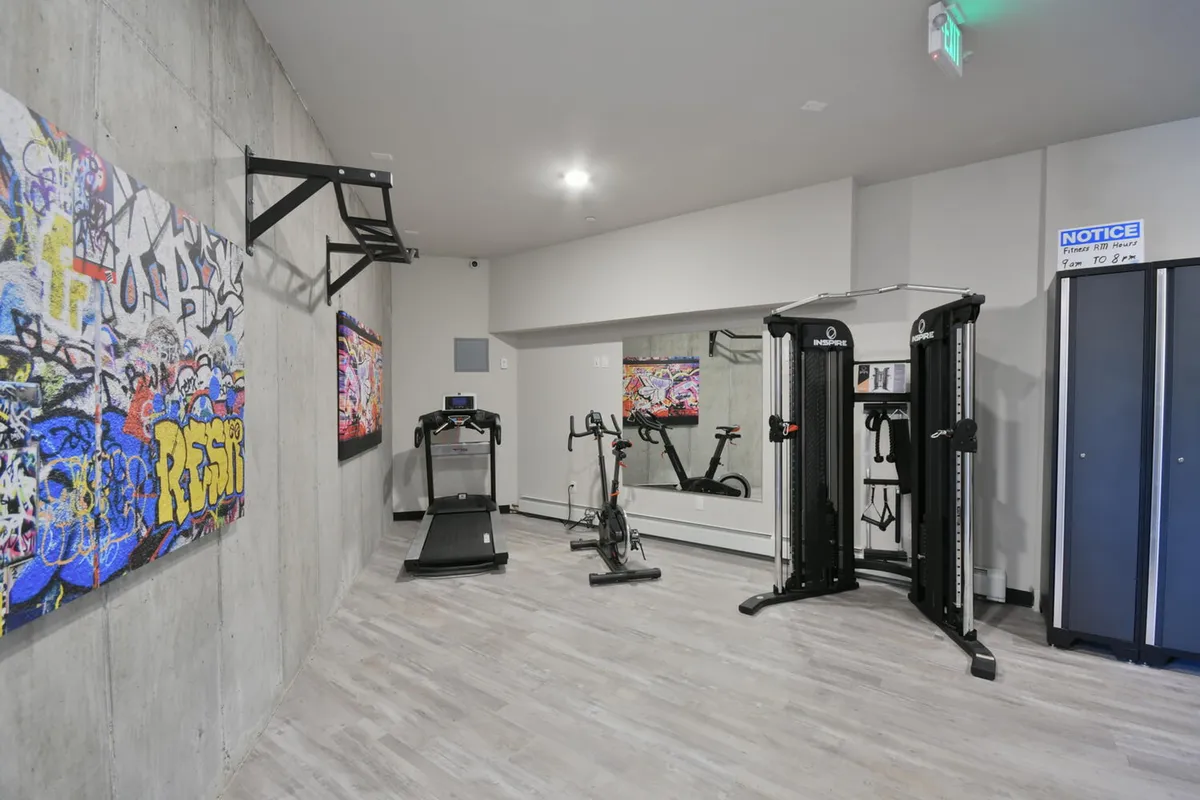 A vibrant, modern gym with a treadmill, stationary bike, cable machine, and motivational graffiti art on the wall. The space is well-equipped for cardio, strength training, and group fitness, promoting an active lifestyle within the property.