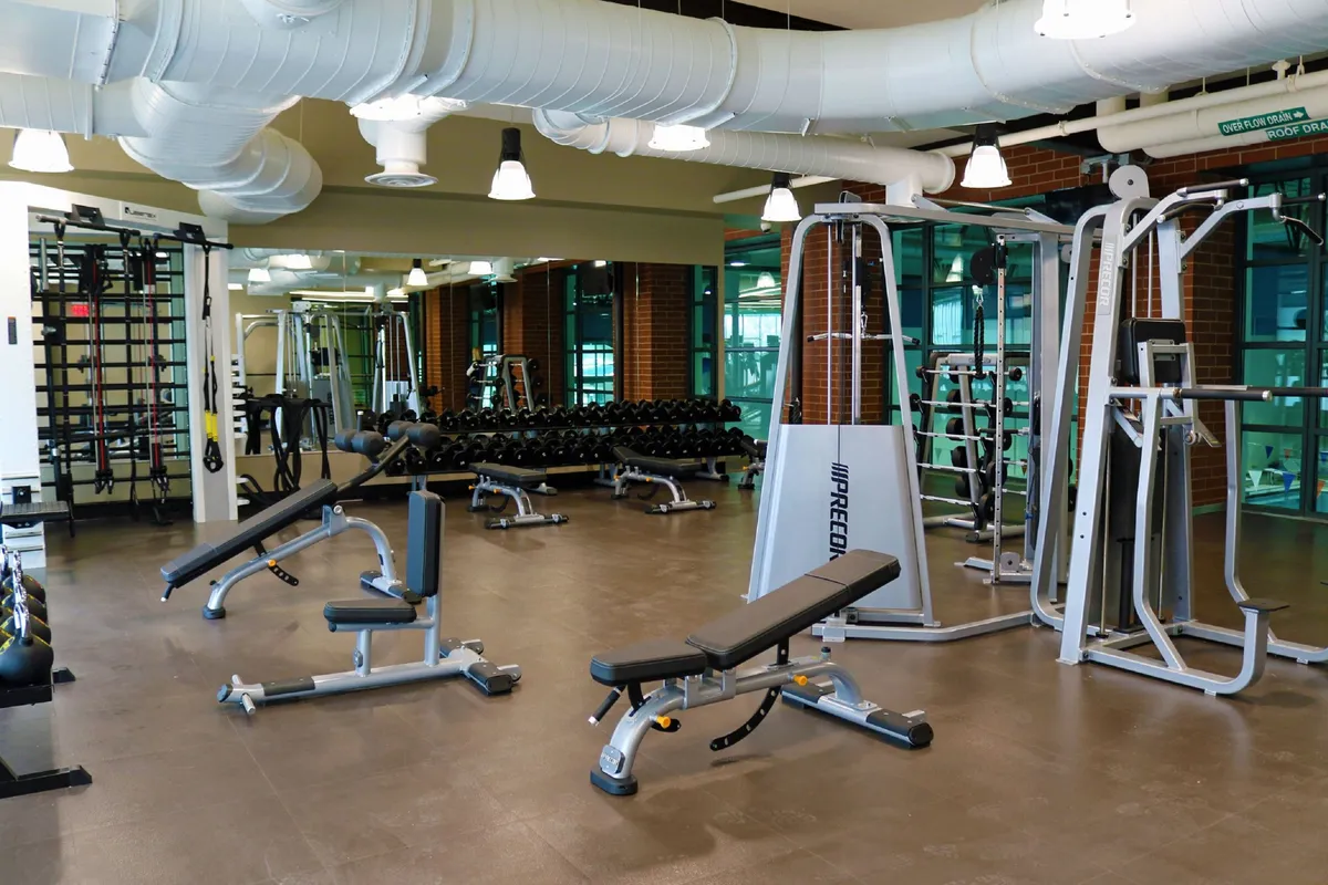 A well-equipped, contemporary fitness center complete with weight benches, dumbbells, and exercise machines. Mirrors line the walls, reflecting a space designed for personal wellness and active lifestyles, embodying the premium amenities mentioned in the narrative.