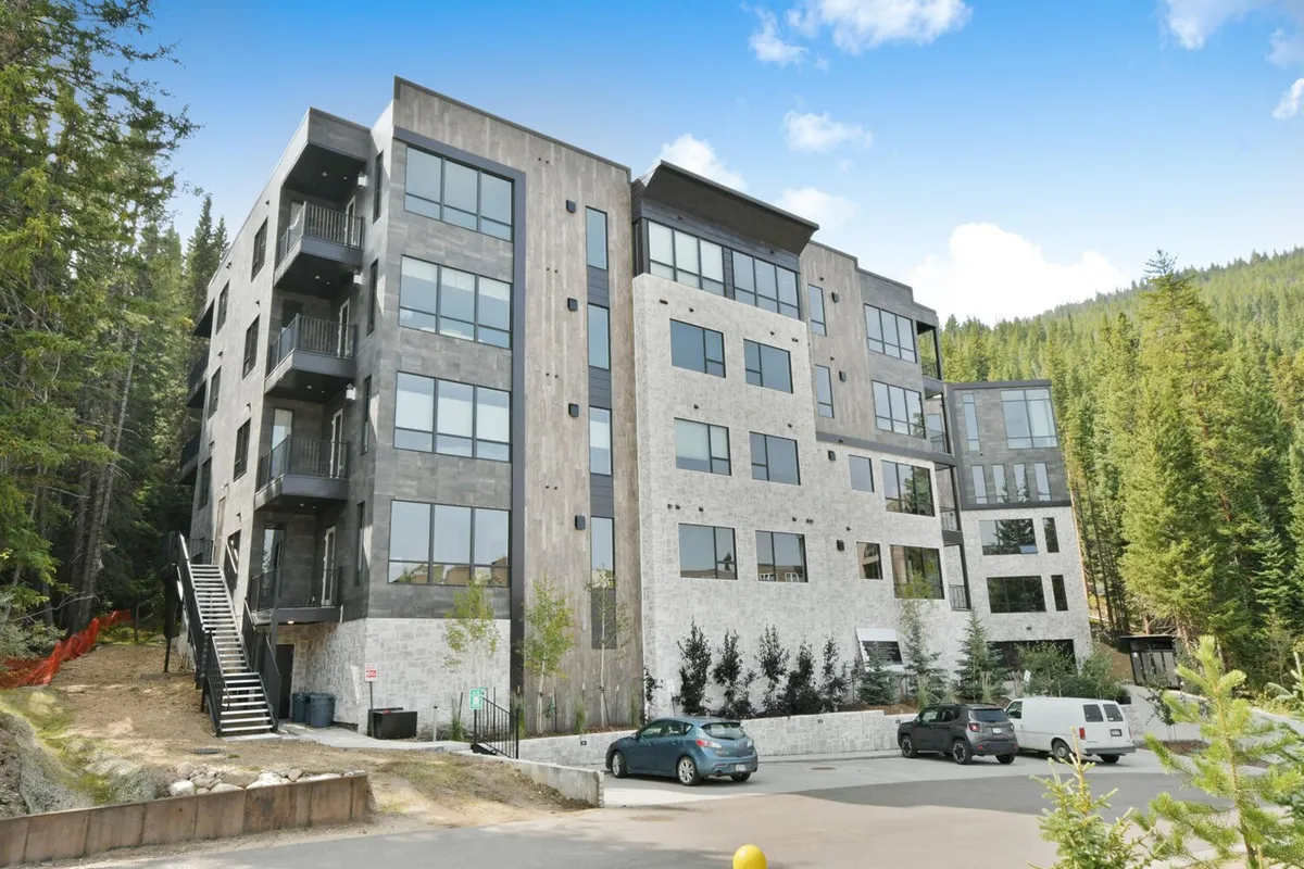 An exterior view of the modern building facade surrounded by tall trees, with large windows looking out into the forest. The scene exudes tranquility and connection to nature, while suggesting forest views promised in the entryway.