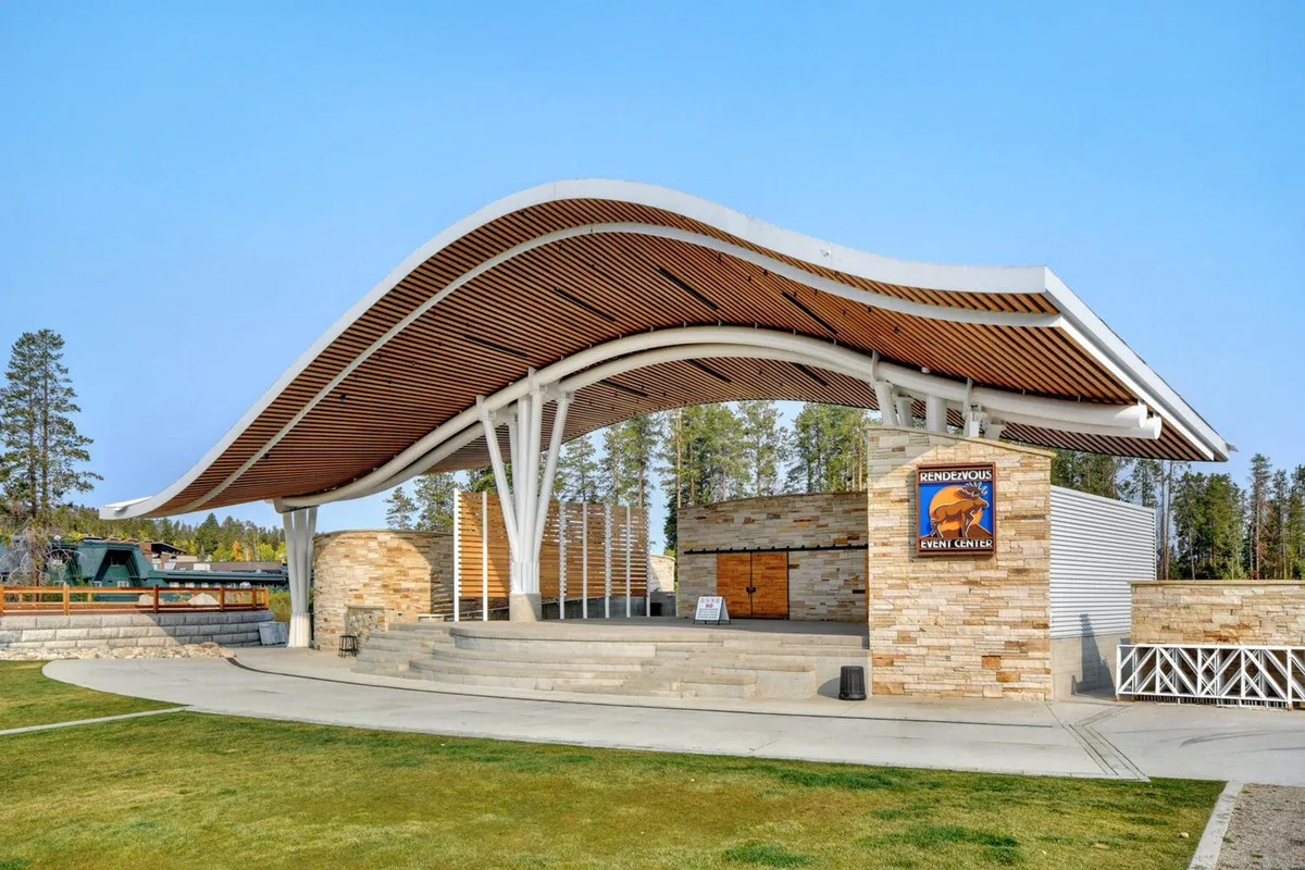 An outdoor community stage area with a curved roof, stone walls, and an open gathering space. The area is set up for performances or movie nights, embodying a sense of communal fun and entertainment.