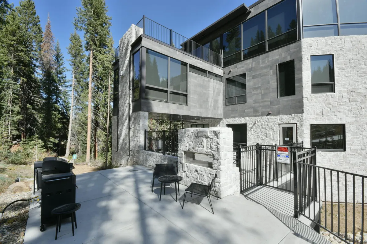 A modern outdoor patio area with comfortable seating, grill, and forest views, seamlessly connecting the inside living areas to the outdoors—perfect for year-round gatherings, morning coffee, or starlit toasts.