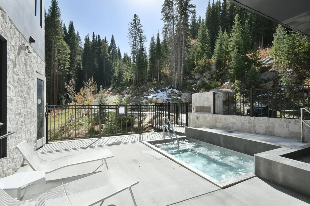 An inviting hot tub set on a deck surrounded by a tranquil forest, with deck chairs for relaxation. The setting exudes peace and is ideal for unwinding after outdoor adventures—whether soaking up morning views or stargazing in the evening.